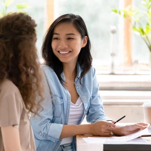Smiling asian hr insurer advisor meeting applicant at job interview consulting client about contract offer giving advice, happy diverse girls colleagues interns students discussing paperwork together